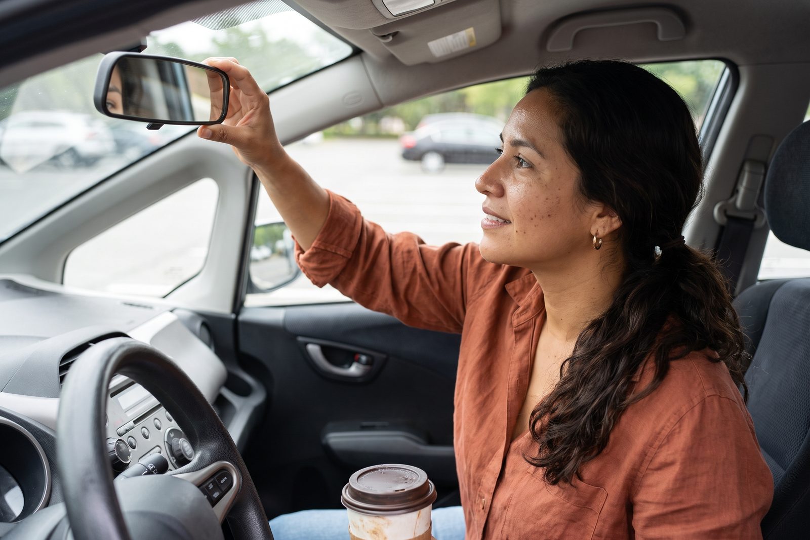 AI-generated illustration of a woman in her 30s in a parked car adjusting the rearview mirror with a slight smile