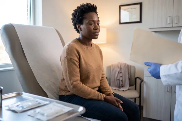 AI-generated illustration of a woman in a knit sweater sitting in a treatment chair, listening to a clinician whose gloved hand holds a folder
