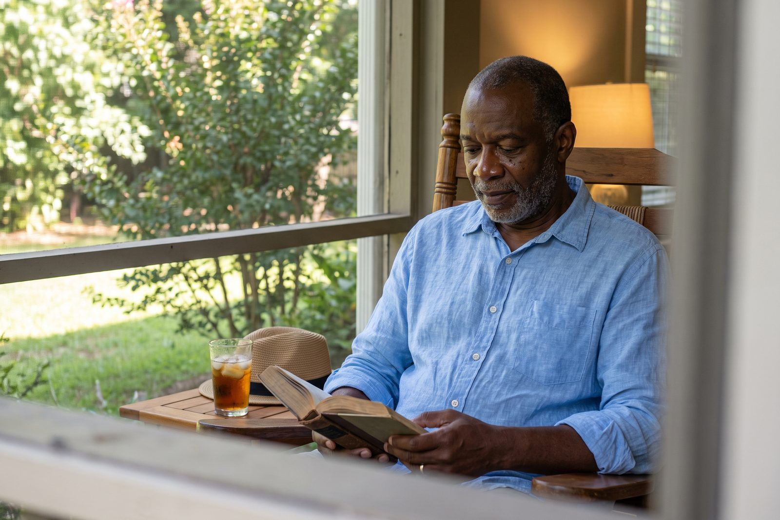AI-generated illustration of a man in his 60s reading in the shade of a screened porch on a sunny summer day