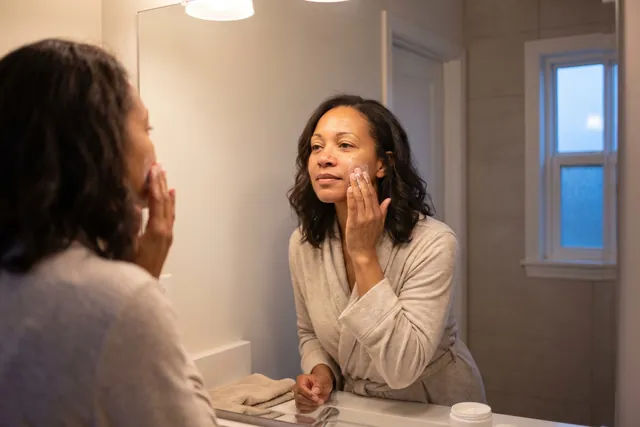 AI-generated illustration of a woman in her 40s gently massaging her cheek in small circles at a bathroom mirror