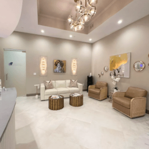 A wide-angle photo of a modern, upscale medical office waiting room featuring plush seating, warm lighting, and a contemporary art piece on the wall
